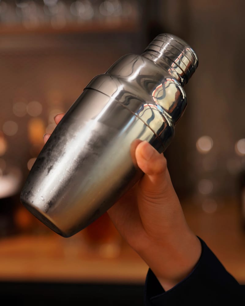 A frosted steel cocktail shaker held up behind a bar.