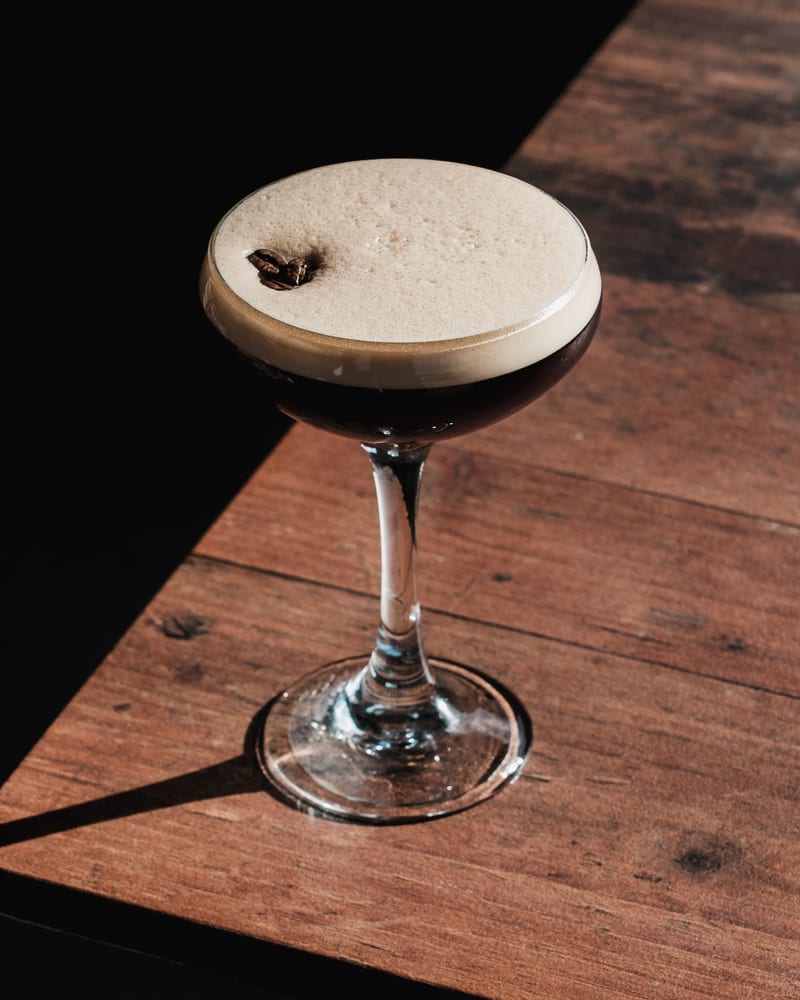 A Demerara espresso martini in a coupe on a wooden table, foam cap topped with coffee beans.